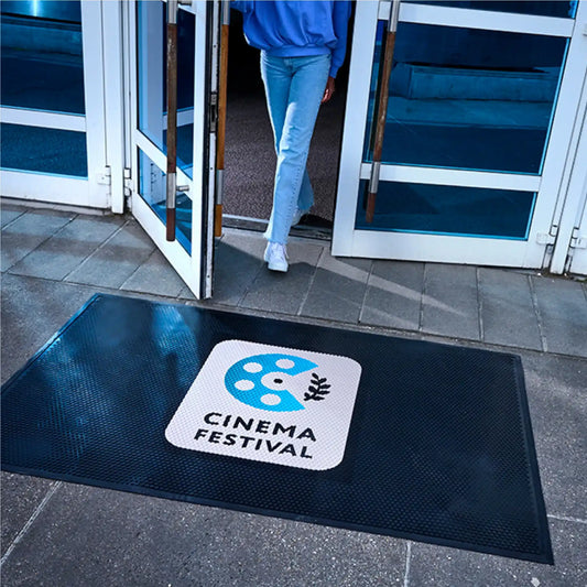 Tapis logo personnalisé en caoutchouc industriel installé devant une entrée pour retenir les saletés et sécuriser les accès.
