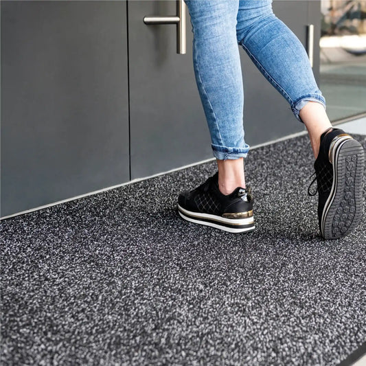 Tapis d’entrée double action grattant absorbant installé devant une porte d’accès pour retenir les saletés et l’humidité.