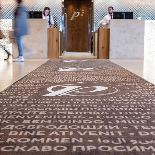 Tapis logo personnalisé grand format XXL placé dans le hall d’accueil d’un hôtel pour accueillir les visiteurs avec élégance.