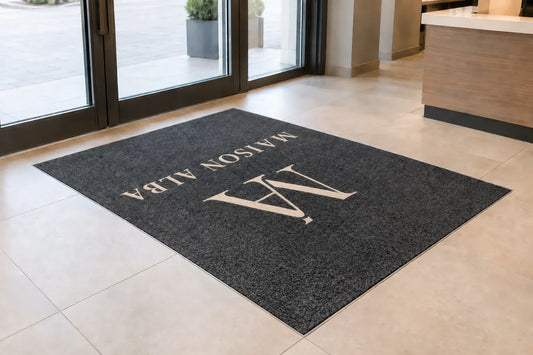 Tapis d’entrée personnalisé sans bordure, encastré dans le sol d’un commerce avec un logo centré.