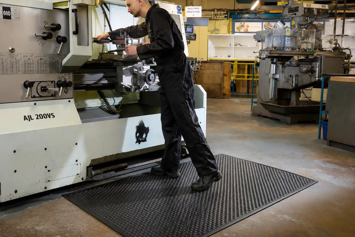 Tapis industriel de sécurité placé devant une machine de production dans un atelier mécanique pour améliorer l'adhérence et le confort des opérateurs