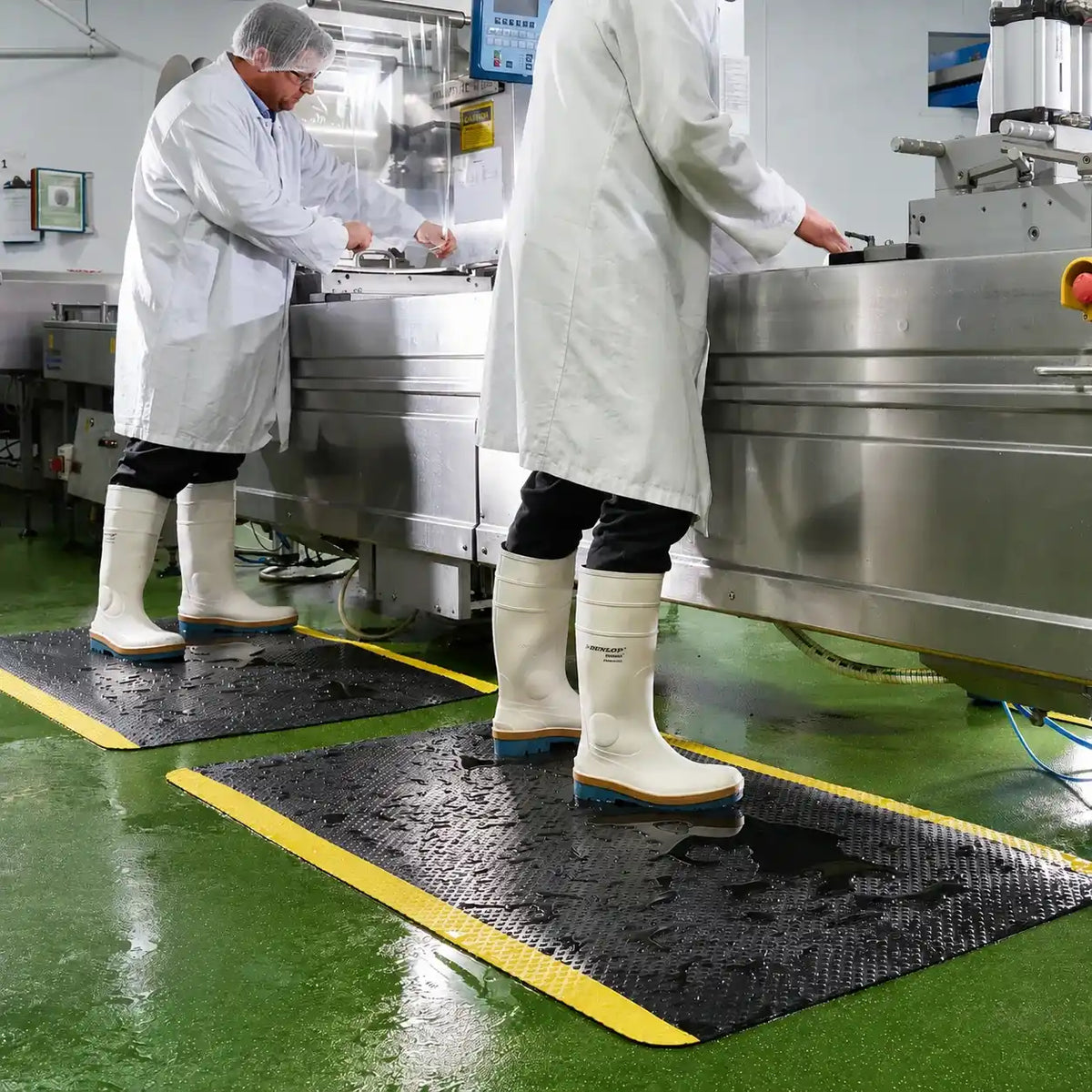 Opérateurs travaillant sur des tapis d'hygiène antidérapants dans une zone de production agroalimentaire avec sol humide