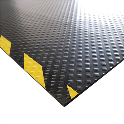 Gros plan sur la surface antidérapante du tapis passe-câbles industriel avec marquage de sécurité jaune et noir haute visibilité.