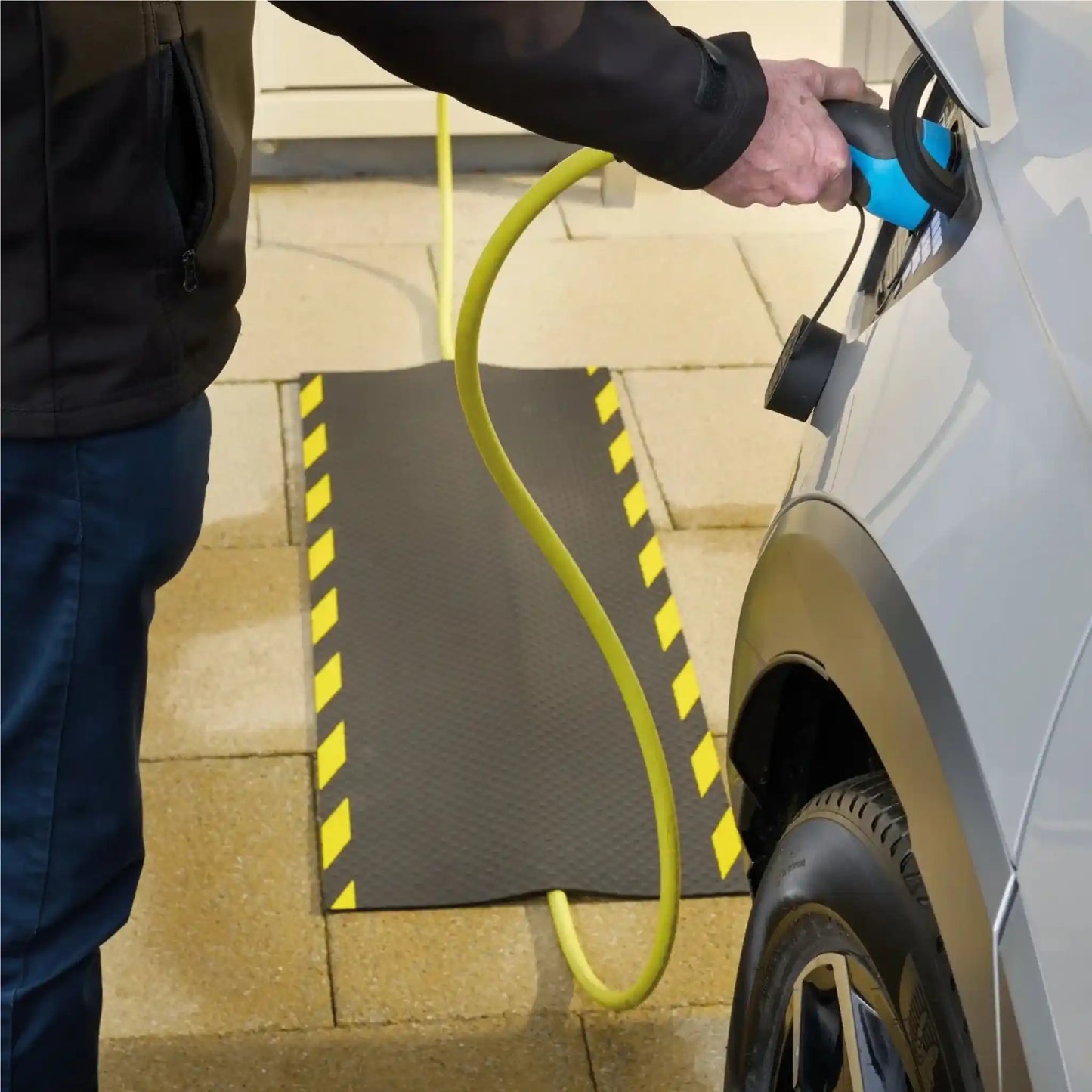 Véhicule électrique en cours de recharge avec câble sécurisé par un tapis de protection robuste pour usage extérieur.