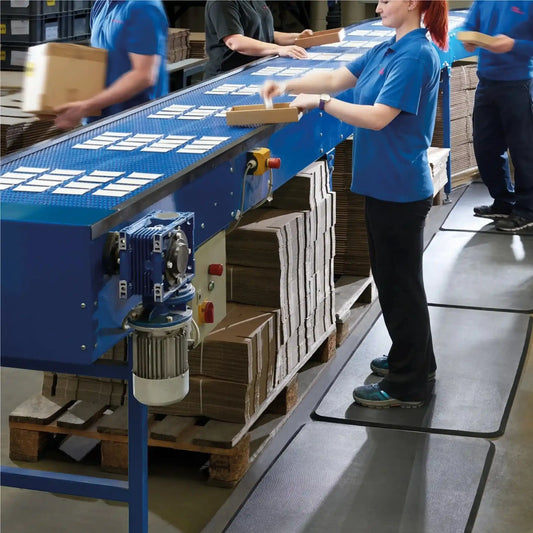 Tapis anti-fatigue professionnel en mousse utilisé sur une ligne de conditionnement pour améliorer le confort des opérateurs debout.