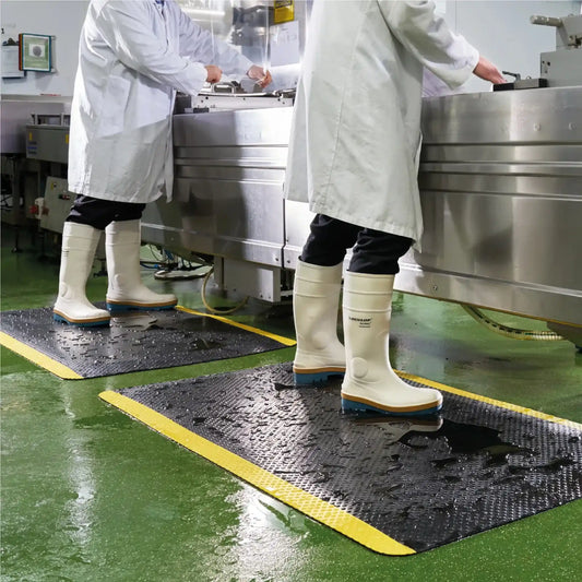 Tapis anti-fatigue professionnel sécurité avec bordures jaunes haute visibilité utilisé dans un environnement agroalimentaire humide.