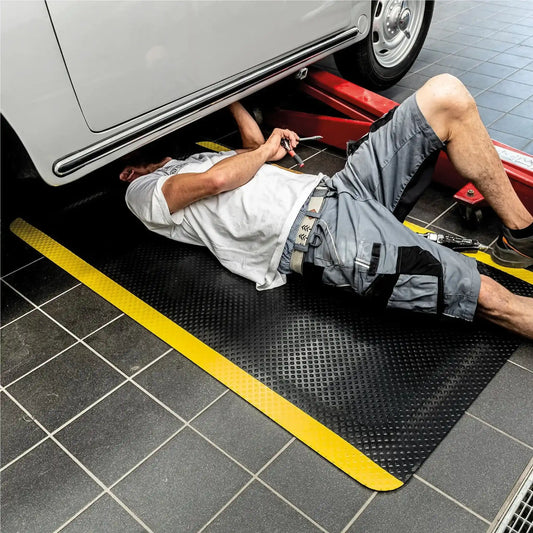 Tapis anti-fatigue professionnel sécurité placé sous un véhicule dans un atelier automobile pour améliorer le confort et la sécurité des mécaniciens.