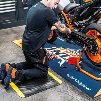 Tapis anti-fatigue professionnel sécurité utilisé pour les travaux à genoux dans un atelier de maintenance moto afin de réduire la pression sur les articulations.