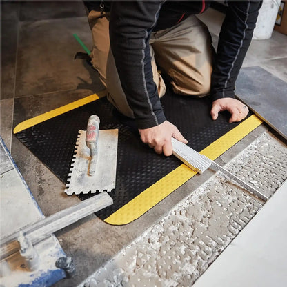 Artisan agenouillé sur un tapis anti-fatigue professionnel sécurité lors d’une intervention technique, offrant un meilleur confort des genoux et une protection contre les sols durs.
