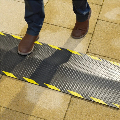 Personne marchant sur un tapis de protection de câble de recharge électrique conçu pour limiter les risques de trébuchement.