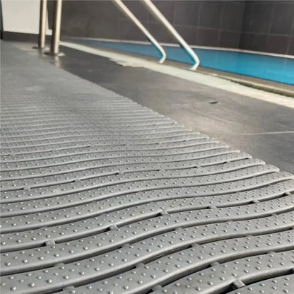 Gros plan sur un tapis drainant antidérapant gris installé aux abords d’une piscine pour limiter les risques de glissade.