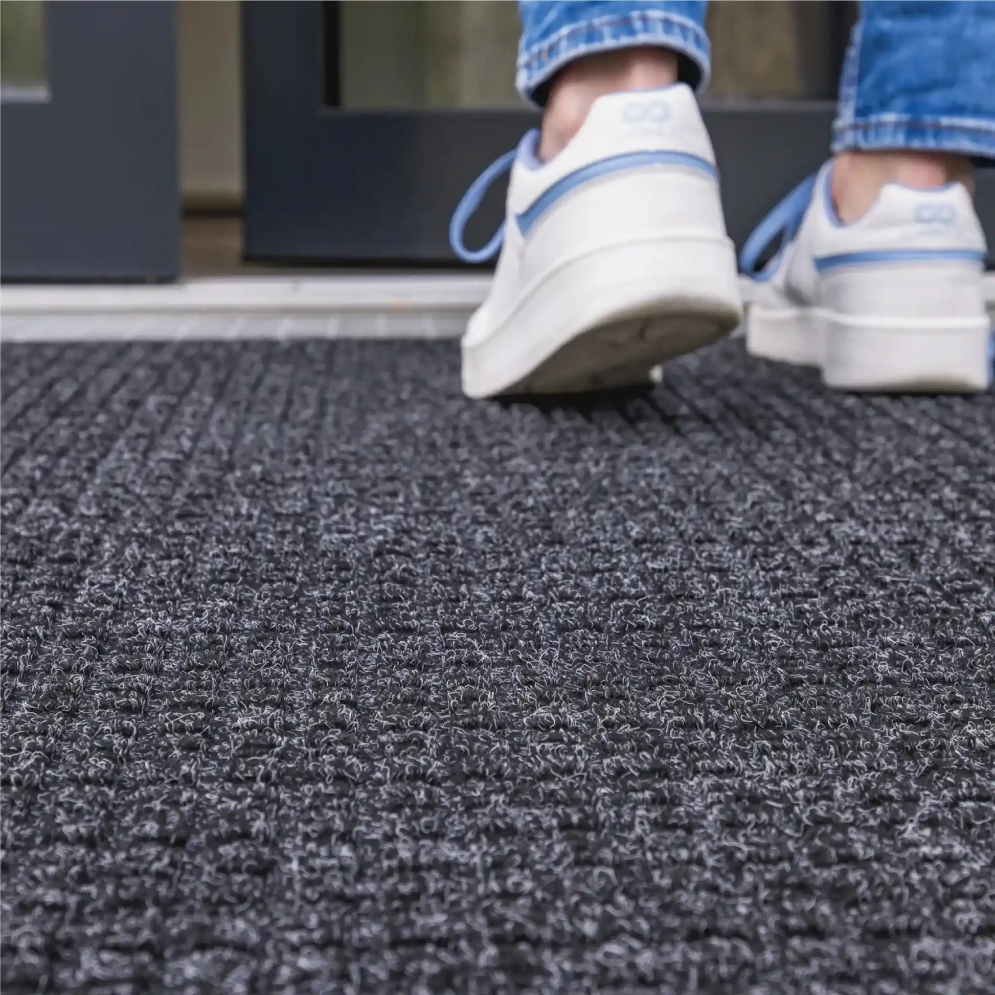 Gros plan sur un tapis d’entrée professionnel absorbant l’eau sous les pas d’un utilisateur entrant dans un bâtiment.