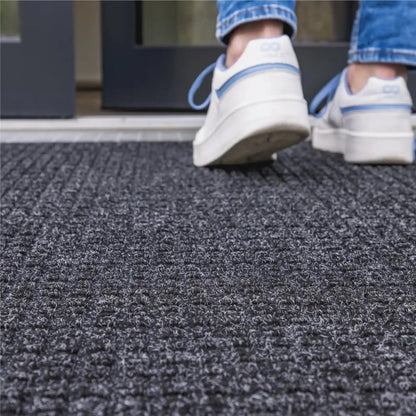 Gros plan sur un tapis d’entrée professionnel absorbant l’eau sous les pas d’un utilisateur entrant dans un bâtiment.