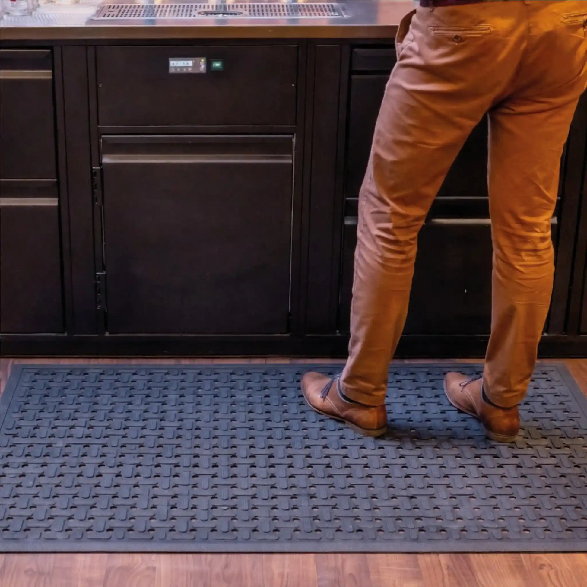 Tapis drainant en caoutchouc placé devant un comptoir de bar afin de réduire la fatigue des jambes et limiter les risques de glissade.