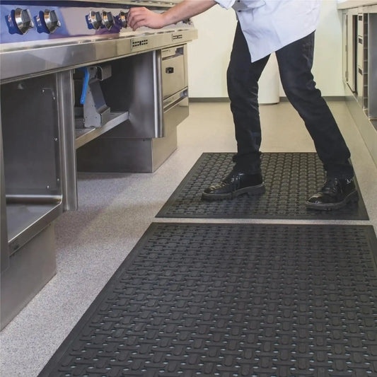 Tapis hygiénique drainant en caoutchouc utilisé dans une cuisine professionnelle pour améliorer le confort, l’adhérence et l’évacuation des liquides au poste de cuisson.