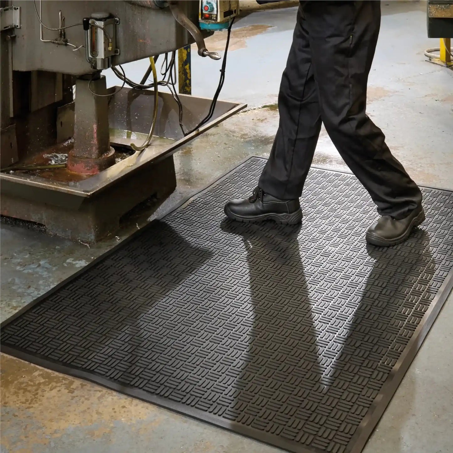 Tapis industriel en caoutchouc pour zones humides placé devant une machine-outil afin d’améliorer l’adhérence, le drainage et le confort des opérateurs.