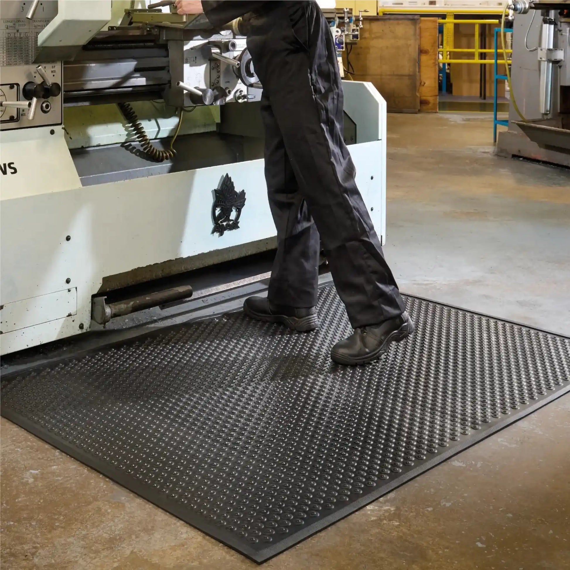 Tapis industriel grattant drainant de sécurité utilisé devant une machine-outil pour améliorer le confort, l’adhérence et la propreté du poste de travail.