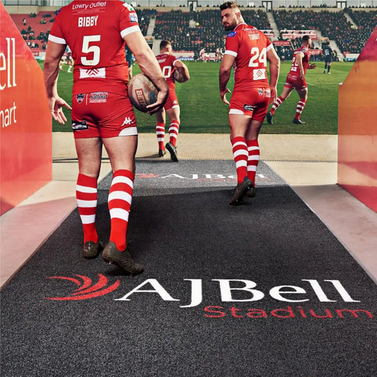 Tapis logo personnalisé effet gazon placé à l’entrée d’un stade sportif pour mettre en avant les sponsors et l’identité visuelle du site.