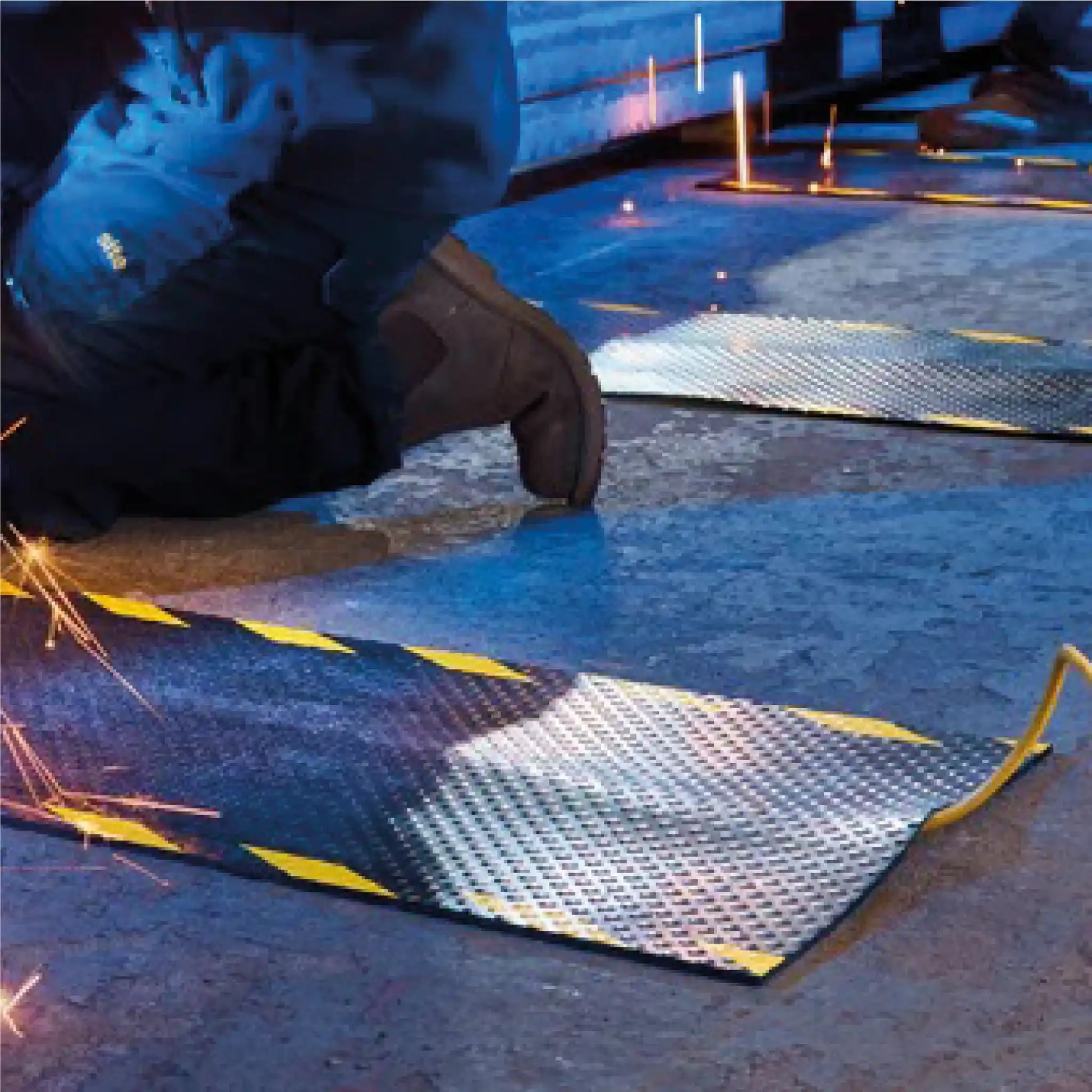 Tapis passe-câbles en caoutchouc utilisé dans un atelier de soudure pour protéger les câbles électriques et réduire les risques de trébuchement.