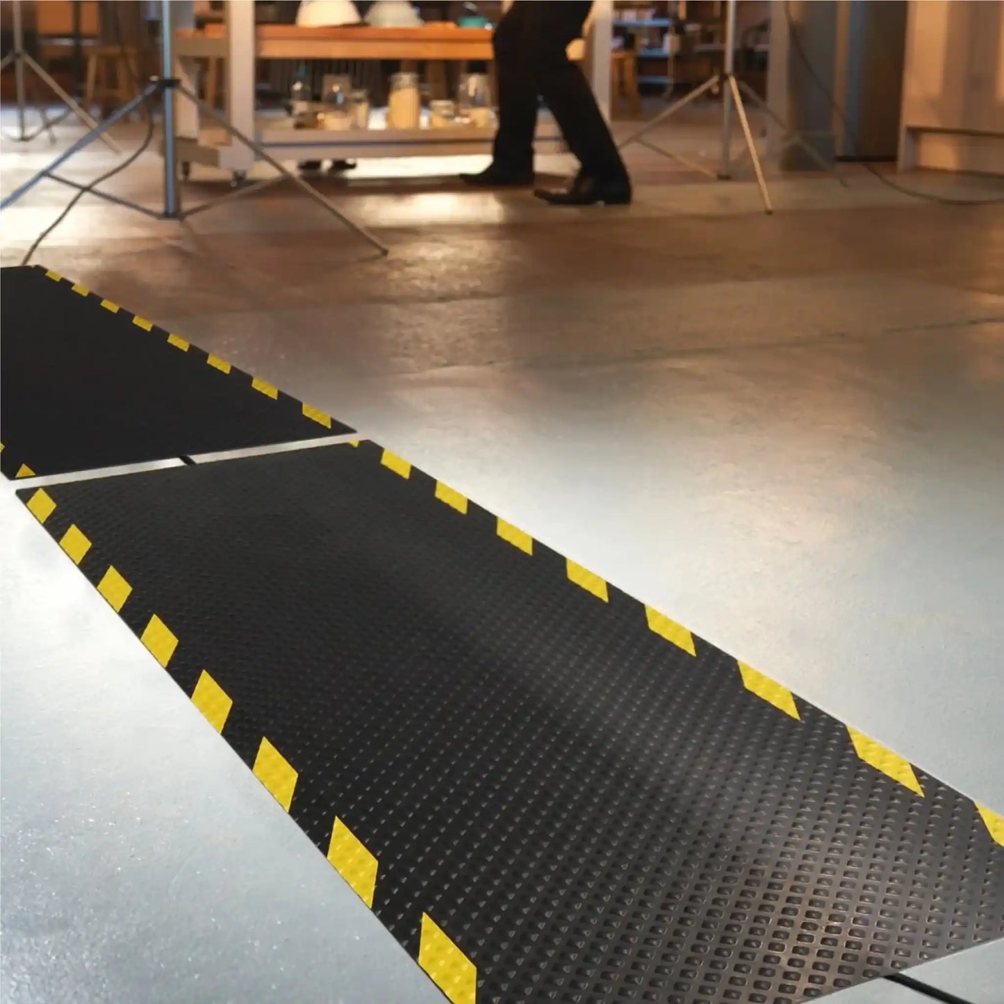 Tapis passe-câbles industriel en caoutchouc installé dans un atelier de production pour protéger les câbles au sol et sécuriser les déplacements du personnel.