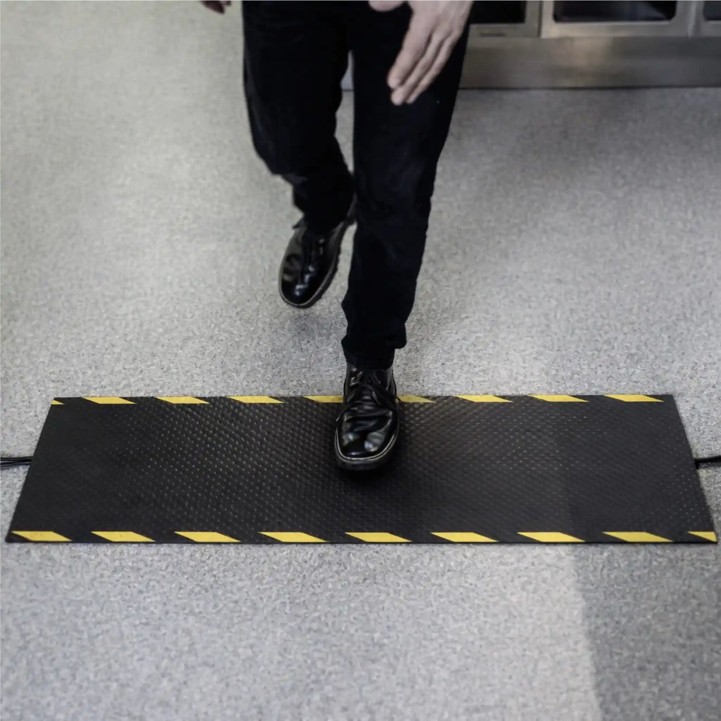 Employé traversant un tapis passe-câbles industriel avec marquage jaune et noir garantissant une visibilité optimale des câbles au sol.
