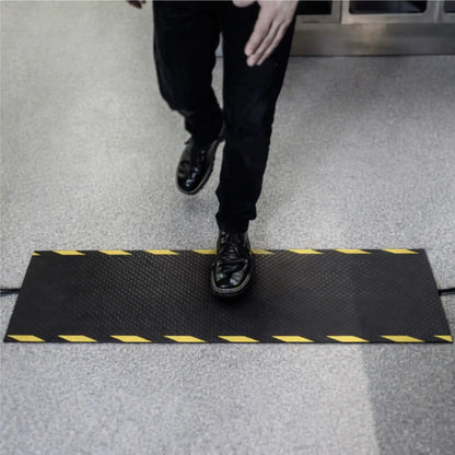 Employé traversant un tapis passe-câbles industriel avec marquage jaune et noir garantissant une visibilité optimale des câbles au sol.