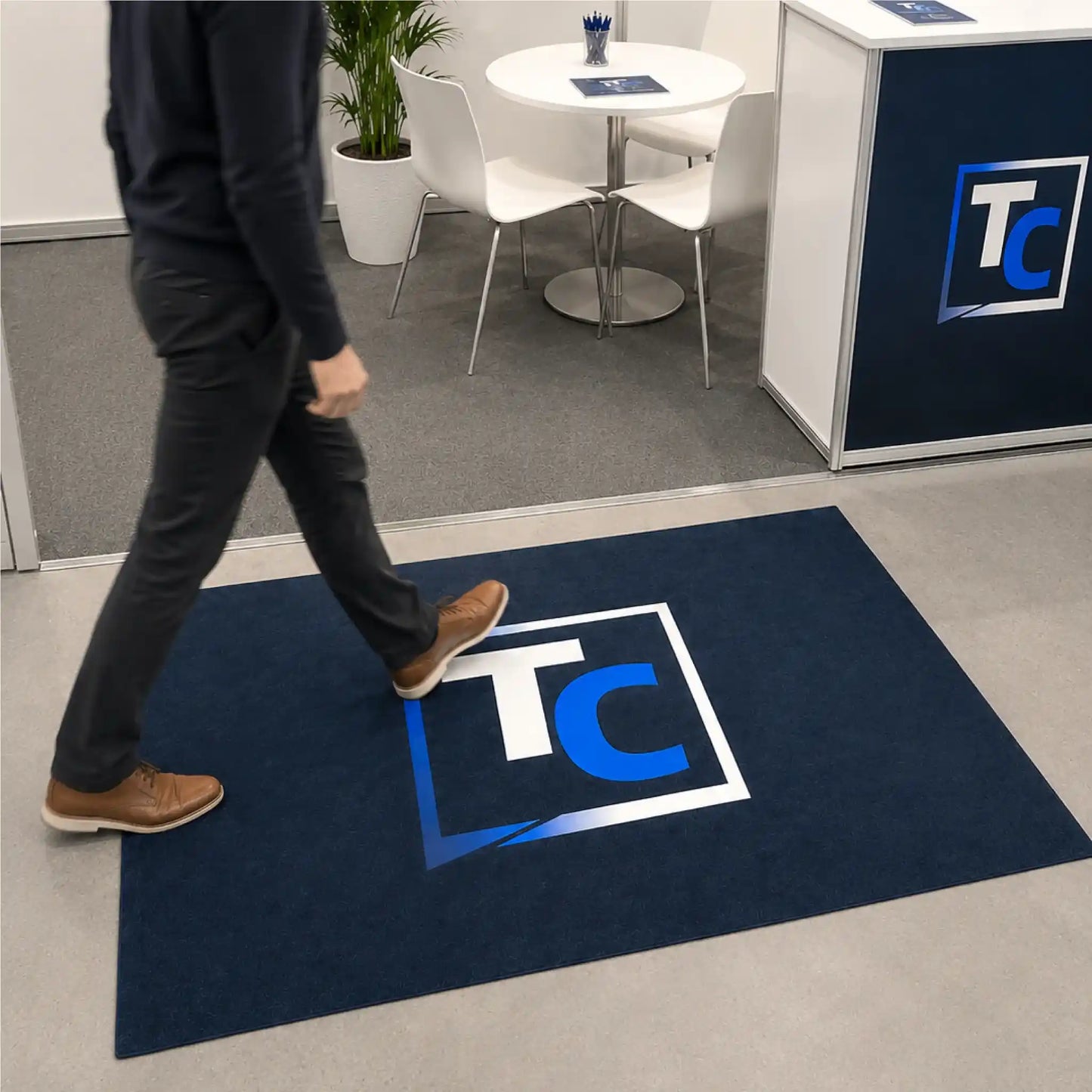Visiteur marchant sur un tapis promotionnel personnalisé sans bordure placé à l’entrée d’un espace d’exposition ou d’accueil.