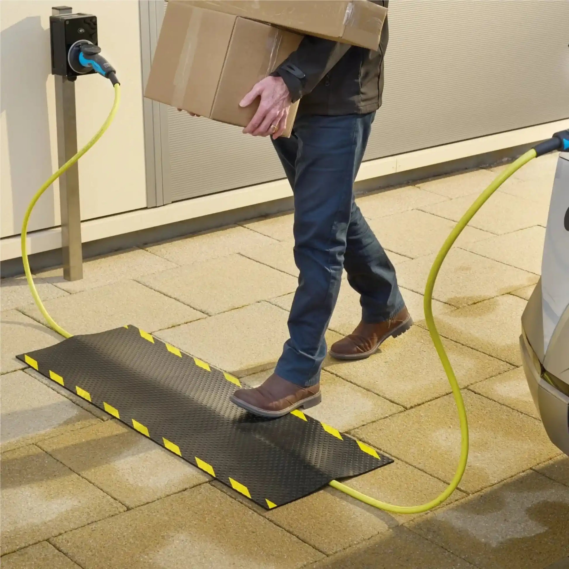Utilisateur franchissant un tapis de protection de câble lors de la recharge d’un véhicule électrique sur une borne extérieure.