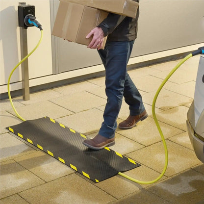 Utilisateur franchissant un tapis de protection de câble lors de la recharge d’un véhicule électrique sur une borne extérieure.